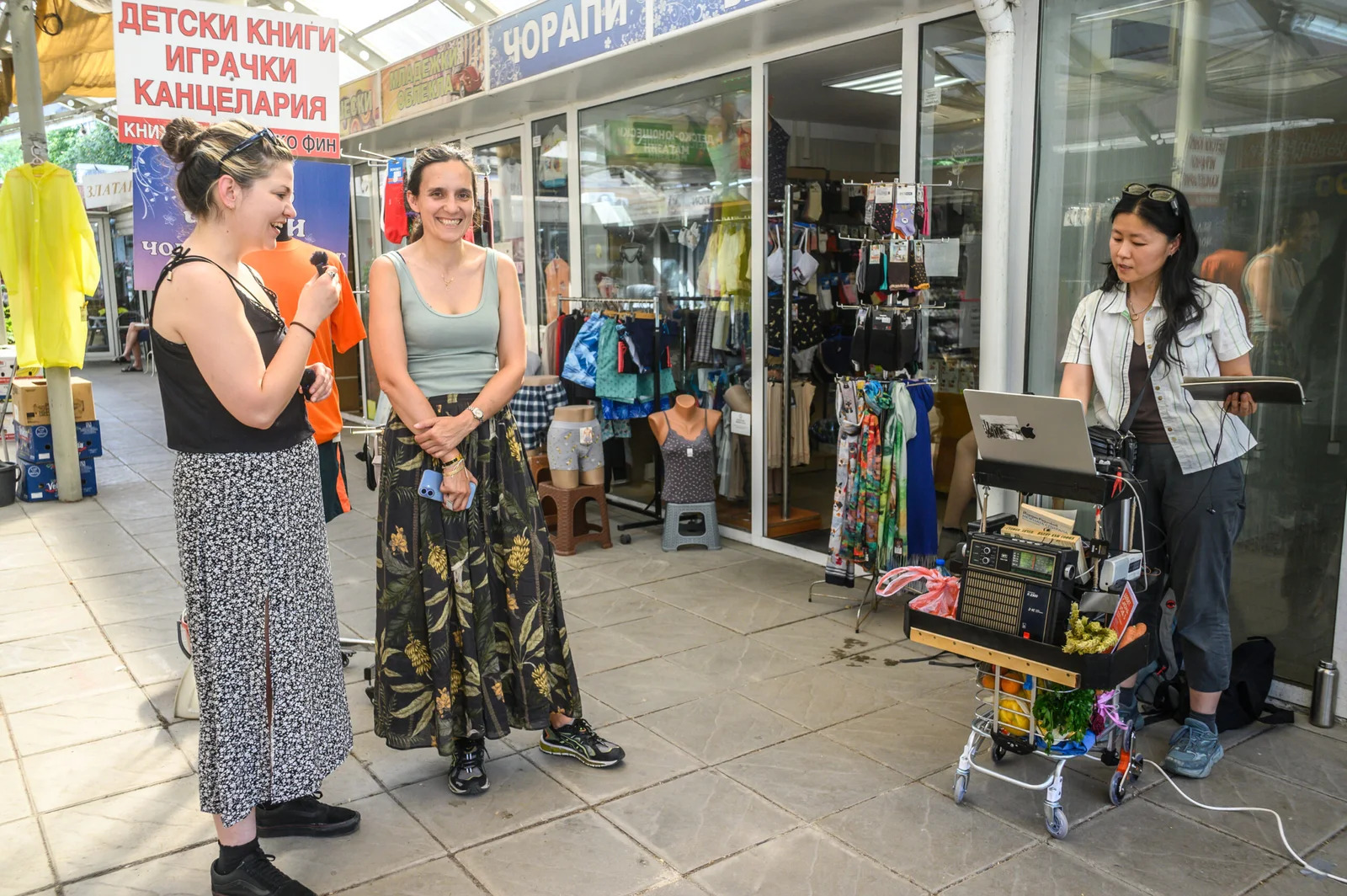 woman interviews woman at a market while radio technician works nearby
